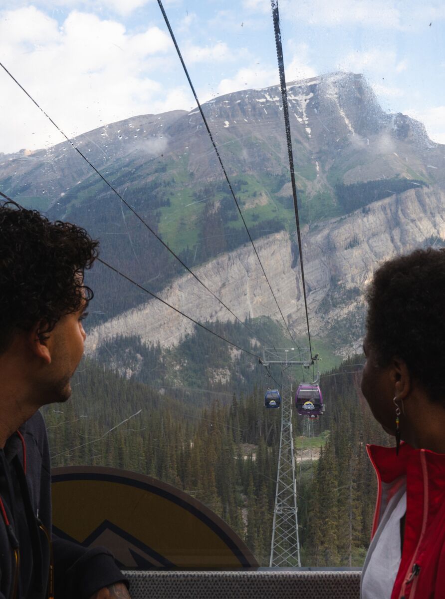 Two people look out of a gondola window towards a mountain at Banff Sunshine Village.
